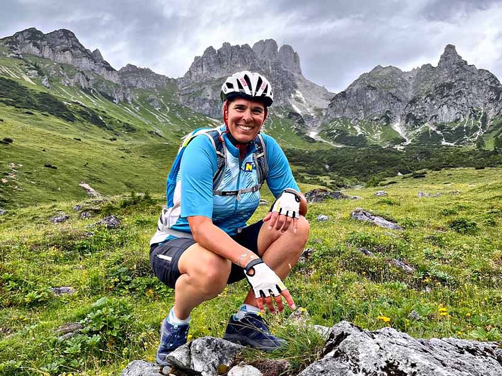 Michaela Dorfmeister auf der Wiese sitzend mit Radhelm im Hintergrund eine Gebirgskette