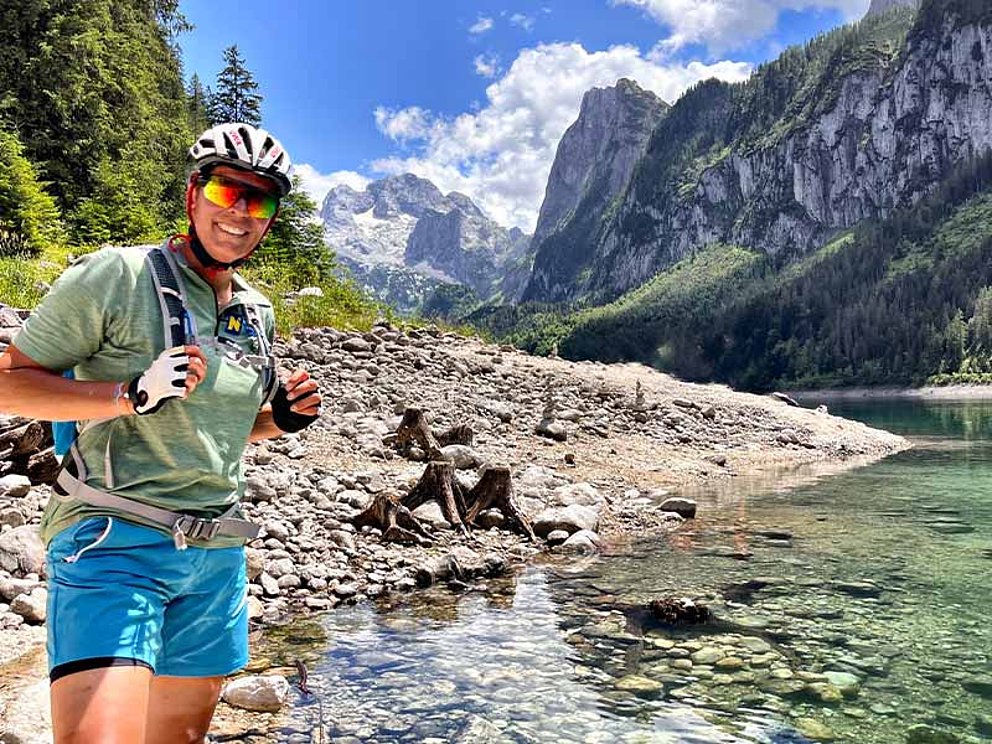 Michaela Dorfmeister mit Radhelm, Rucksack und Sonnenbrille im Hintergrund der Dachstein und der Gosausee