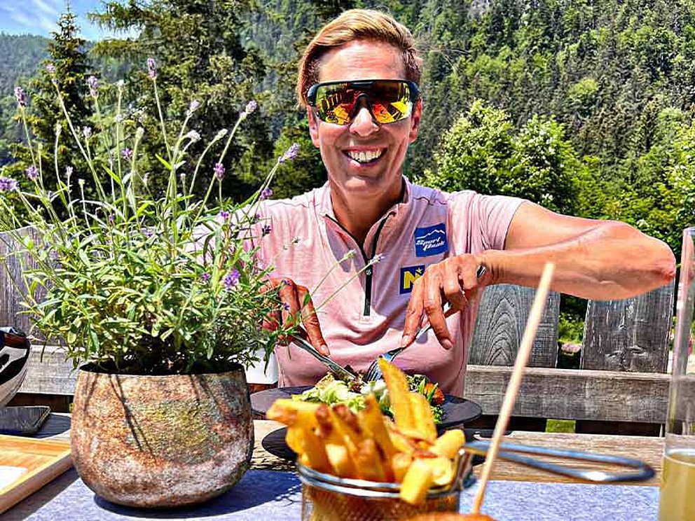 Michaela Dorfmeister strahlend mit Sonnenbrille vor vollen Tellern