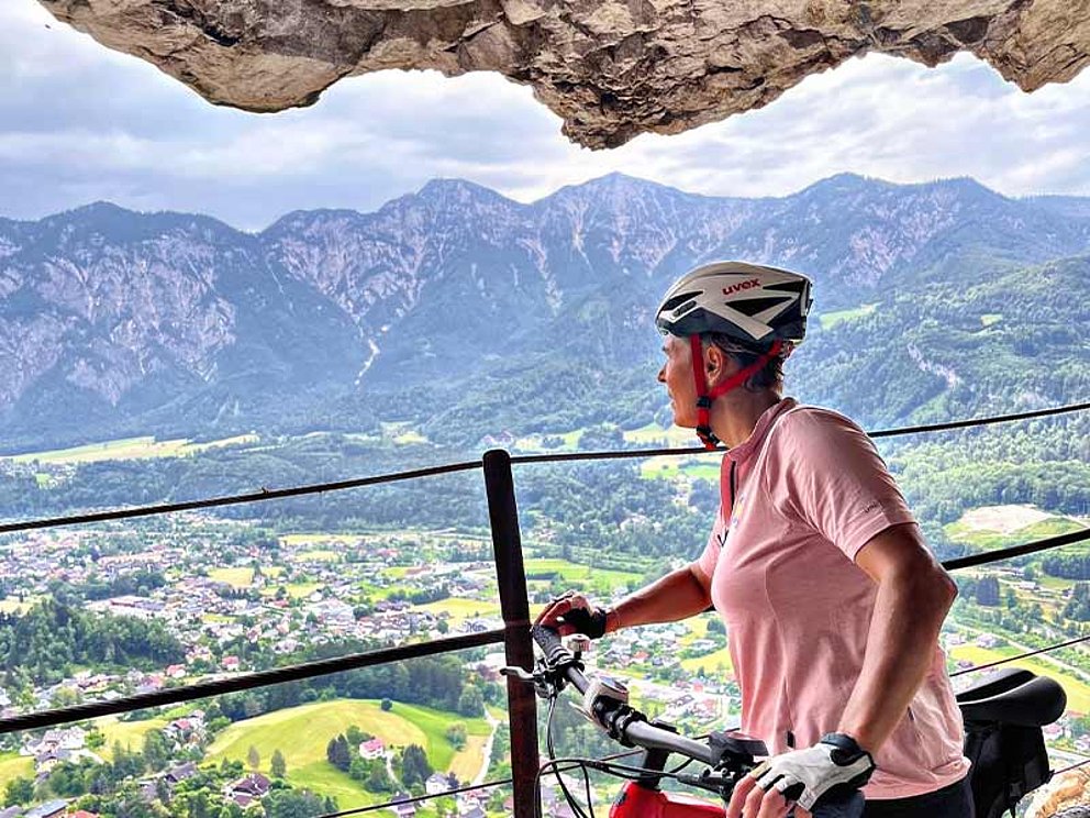 Michaela Dorfmeister von der Seite am Rad sitzend, im Hintergrund das Geländer der Ewigen Wand, Berpanorma und Bad Goisern