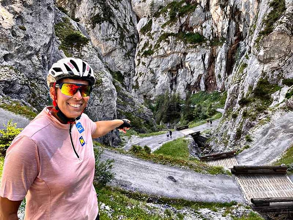 Michaela Dorfmeister mit Radhelm und Brille zeigt auf den darunter liegenden Schotterweg bei den Öfen