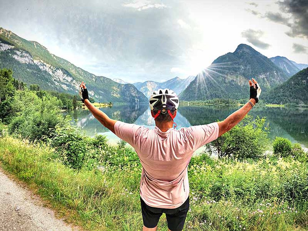 Michaela Dorfmeister von hinten mit einer die Landschaft umarmenden Geste, im Hintergrund ein Bergsee und Bergpanorama