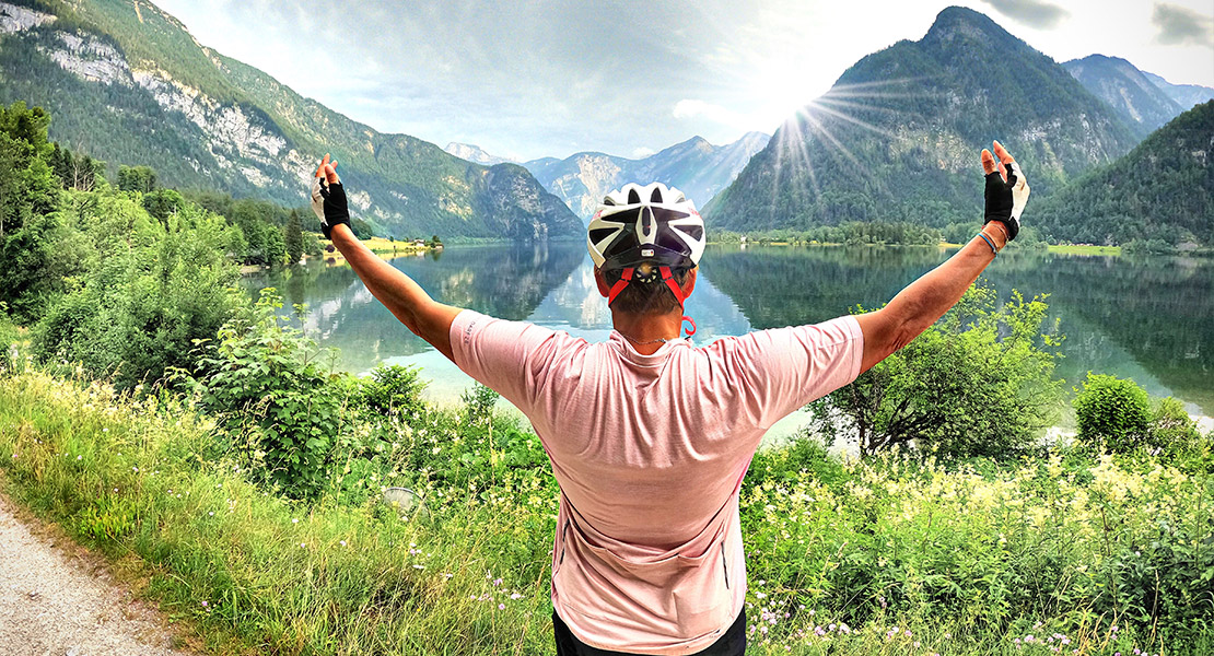 Michaela Dorfmeister von hinten mit einer die Landschaft umarmenden Geste, im Hintergrund ein Bergsee und Bergpanorama